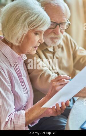 Primo piano di una coppia senior preoccupata che controlla il proprio account a casa mentre si tengono documenti. Concetto di famiglia e di famiglia Foto Stock