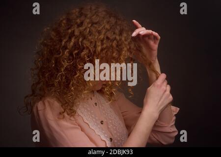 Studio ritratto di una giovane donna con capelli ricci. Gioca con una ciocca di capelli. Il concetto di cura e la salute dei capelli Foto Stock