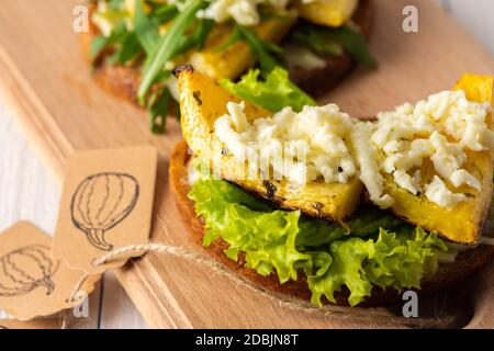 Panini tostati con formaggio brie, zucca al forno e insalata, rucola e mozzarella, deliziosi spuntini vegetali su tavola di legno Foto Stock
