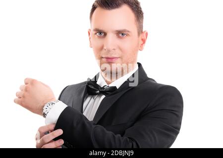 Ritratto di un giovane sicuro e attraente in abito nero con cravatta ad arco, regolando i gemelli sulla sua camicia bianca, guardando la fotocamera, isolato o Foto Stock