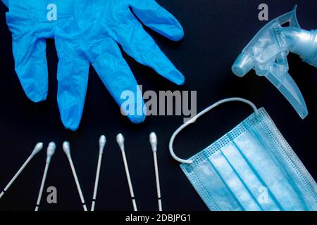 Un primo piano di articoli medici: Tamponi alla gola, guanti, maschera medica per il viso e spray disinfettante spray liquido spray su sfondo nero. Foto Stock