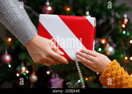 La mamma dà al bambino un regalo sullo sfondo di un albero di Natale con luci. Foto Stock