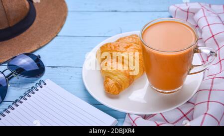 Tè al latte in vetreria e pane integrale con un taccuino e occhiali da sole. C'è una spiaggia sul tavolo di legno blu del Patel. Festa latte tè rela Foto Stock