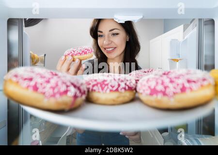 Happy giovane donna che prende Donut da frigorifero o congelatore Foto Stock