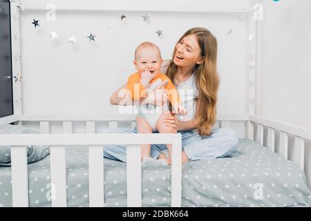 bella madre, che tiene un ragazzino fra le braccia, seduta sul letto di un bambino, la mamma si svegliò con un bambino, la stanza dei bambini Foto Stock