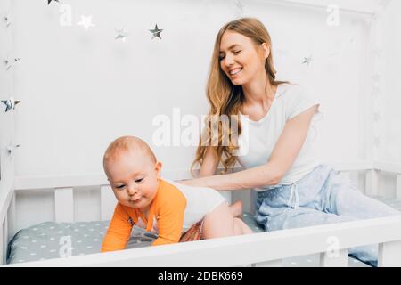 bella madre, che tiene un ragazzino fra le braccia, seduta sul letto di un bambino, la mamma si svegliò con un bambino, la stanza dei bambini Foto Stock