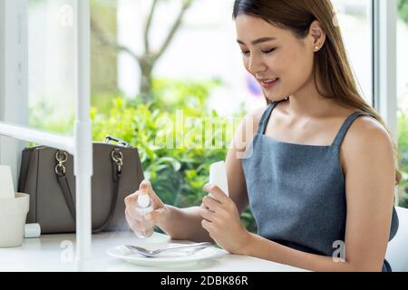 Asian attraente donna che spruzzano alcool su stoviglie in ristorante per pulire ridurre l'infezione di coronavirus covid-19. Nuovo stile di vita normale al restau Foto Stock