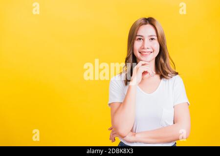 Ritratto Asian Thai bella giovane donna che indossa la t-shirt bianca in piedi manico mento rilassato pensare a qualcosa di circa la domanda studio shot, Foto Stock