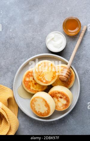 Cheesecake, frittelle di formaggio o Syrniki. Tradizionale russo, ucraino prima colazione pasto. Frittelle al formaggio fritte servite con miele e panna acida Foto Stock