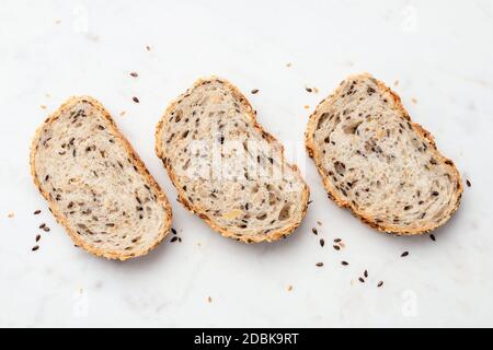 Fette di pane multigrein su sfondo di marmo, vista dall'alto. Pane sano con semi Foto Stock