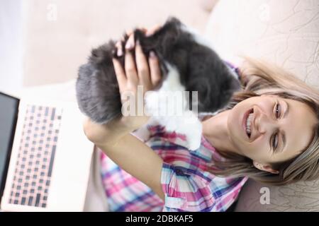 Una donna sorridente è seduta sul divano e tiene il gatto. Foto Stock