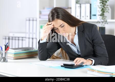 La donna che controlla la calcolatrice è preoccupata, è seduta su una scrivania in ufficio Foto Stock