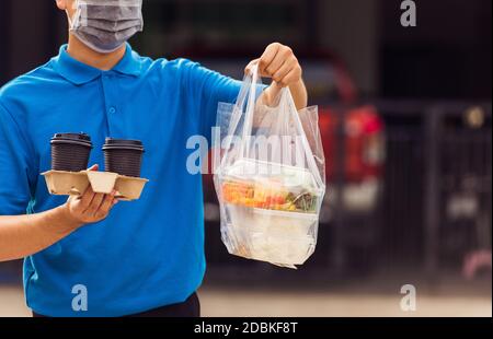 Giovane uomo asiatico di consegna in uniforme blu maschera di indossare faccia servizio di drogheria che dà riso scatole di plastica sacchetti di cibo e caffè in casa davanti sotto Foto Stock