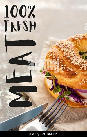 saporito bagel con carne su tovagliolo con posate quasi fresche scritte di carne su superficie testurizzata Foto Stock