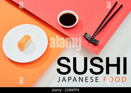 nigiri freschi con salmone vicino alla salsa di soia, bastoncini e sushi giapponese cibo scritta su superficie rossa, arancione, bianca Foto Stock