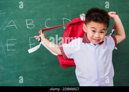 Ritorno a scuola. Felice asiatico divertente cute bambino ragazzo asilo preschool in uniforme studente che indossa borsa scuola stand sorridente su scuola verde bla Foto Stock