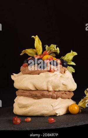 Dessert Pavlova su sfondo nero. Torta Pavlova guarnita con panna montata e frutta mista. Foto Stock