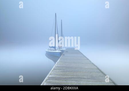 barche sul grande lago in nebbia crepuscolo dal molo Foto Stock