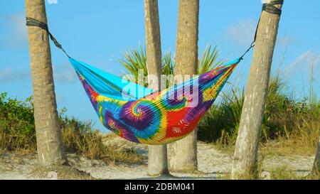 Amaca di colori arcobaleno appesa tra le palme sulla spiaggia. Persone in vacanza estiva relax in amaca. Foto Stock