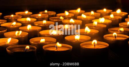 Candele che bruciano. Profondità di campo poco profonda. Molte candele di natale che bruciano di notte. Sfondo astratto candele. Molte fiamme di candela che si illuminano sulla parte posteriore scura Foto Stock