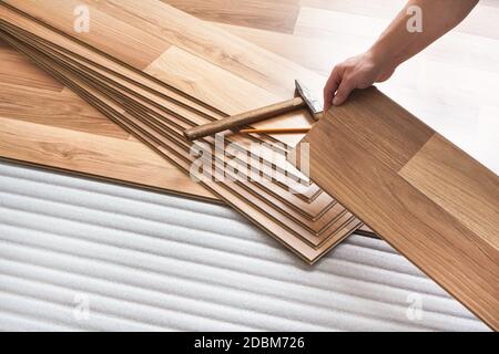 Installazione del pavimento laminato, dettaglio sulle mani dell'uomo che reggono la piastrella di legno, sopra lo strato di base di schiuma bianco. Foto Stock