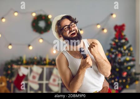 L'uomo nel cappello di Natale canta le canzoni di Natale nel microfono ad una festa del karaoke a casa. Foto Stock