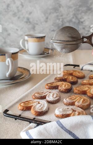 Una signora spolverare lo zucchero in polvere da un irrigatore sopra i biscotti. Biscotti con zucchero in polvere. Foto Stock