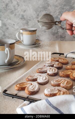 Una signora spolverare lo zucchero in polvere da un irrigatore sopra i biscotti. Biscotti con zucchero in polvere. Foto Stock