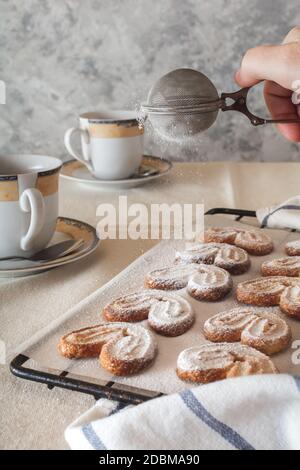 Una signora spolverare lo zucchero in polvere da un irrigatore sopra i biscotti. Biscotti con zucchero in polvere. Foto Stock