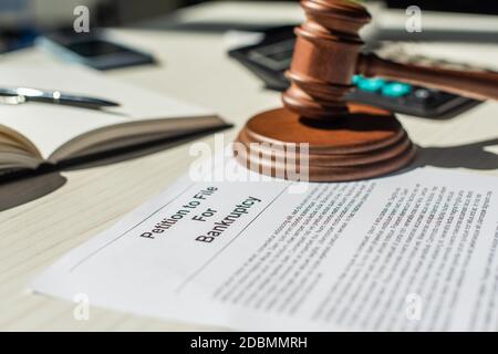 Primo piano vista della gavel e del blocco di legno su petizione per il fallimento sul tavolo con cancelleria offuscata sullo sfondo Foto Stock