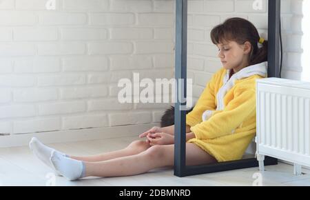 La ragazza triste si siede sul pavimento sotto il tavolo, il gatto dorme vicino Foto Stock