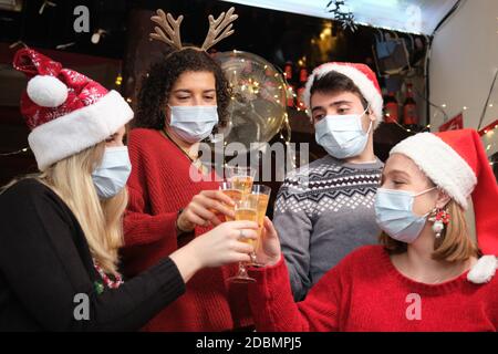 Gli amici indossano maschere per il viso durante una festa di Natale facendo un brindisi in un bar. Coronavirus nuovo normale. Foto Stock