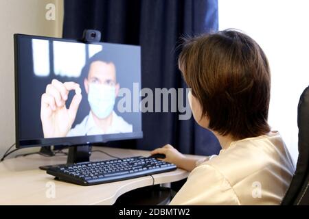 Consultazione online con un medico, donna ascolta le raccomandazioni del medico seduto di fronte alla webcam del PC. Uomo in maschera medica con pillola Foto Stock