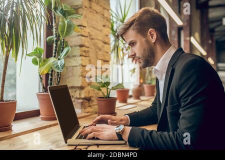 Giovane uomo d'affari che lavora sul portatile in un bar e. aspetto concentrato Foto Stock