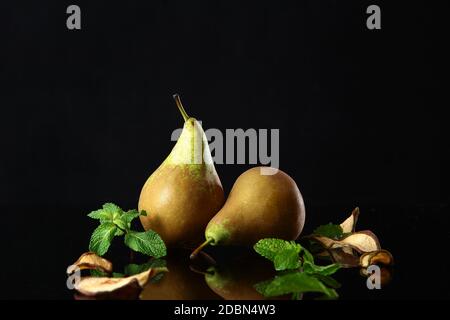 2 pere verdi mature su fondo nero con menta e fette di frutta secca. Foto con riflesso di frutta. Concetto di vita still. Spazio di copia. Foto Stock