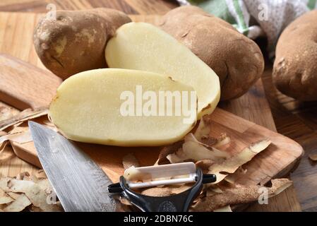 Patate Russet essendo pelato e tagliato su un tagliere Foto Stock