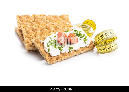 Knackebrot e nastro di misurazione. Pane croccante con formaggio cremoso, pomodori ciliegini e erba cipollina isolati su fondo bianco. Foto Stock