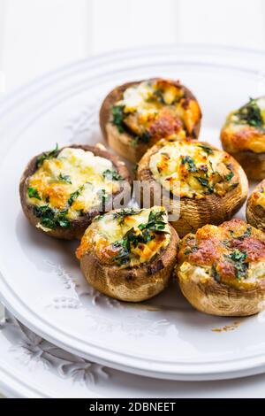 Funghi di champignons al forno, ripieni di formaggio, prezzemolo e aglio arrostito su piatto bianco. Messa a fuoco selettiva. Concetto di cibo sano. Foto Stock