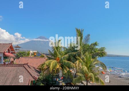 Paradiso tropicale con palme e maestoso vulcano in background. Nuvole bianche attorno al cratere di un vulcano. Vista da sopra i tetti della casa Foto Stock