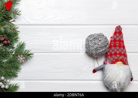 Rami di pino con fiocco di neve e ornamenti di mitten, gnomo di Capodanno con palla d'argento su sfondo di legno bianco. Modello, spazio di copia Foto Stock