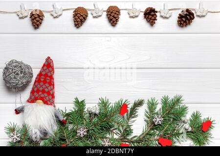 Gnomo di Capodanno con palla d'argento, rami di pino con ornamenti di mitten e fiocco di neve, ghirlanda con coni e angeli. Modello poster, spazio di copia Foto Stock