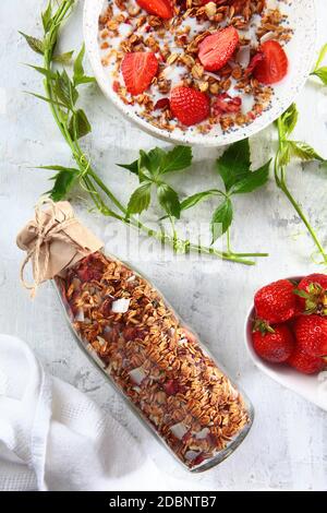 Colazione a base di cereali secchi e fragole con latte. Granola in una bottiglia di vetro su uno sfondo chiaro. Il concetto di una colazione sana. Spazio di copia. Foto Stock