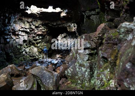 Un giovane che indossa una giacca blu prende un momento per esaminare il percorso roccioso che si trova davanti al tunnel di Raufarholshellir Lava in Islanda. Foto Stock