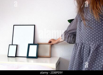 Donna con foto o cornice vuota in una stanza moderna vicino a parete bianca, design scandinavo, spazio interno retrò per il testo Foto Stock