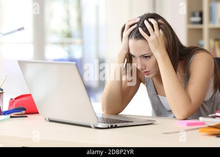 Donna studentesca stressata che si ricorda di un computer portatile che studia seduto su una scrivania a casa Foto Stock