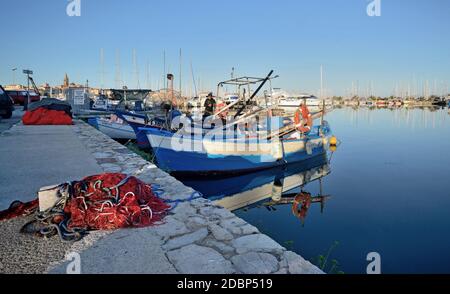 un assaggio del porto poco dopo l'alba con il reti di pescatori sul molo e la città nel sfondo Foto Stock