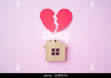 Divorzio, divisione della proprietà, povertà e nessun concetto di denaro. Casa di legno con cuore rotto su sfondo rosa brillante. Ipoteca, affitto, realtor Foto Stock