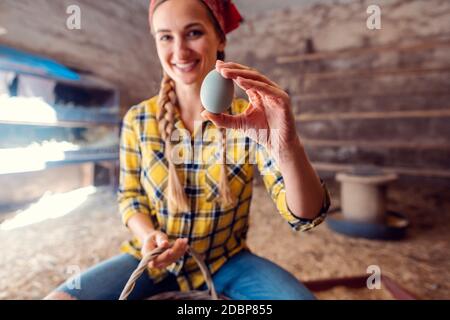 Donna contadina felice mostrando uovo che ha appena raccolto in un henhouse Foto Stock