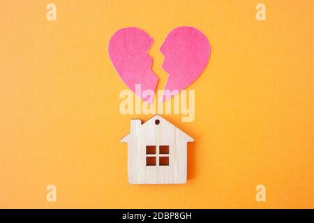 Divorzio, divisione della proprietà, povertà e nessun concetto di denaro. Casa di legno con cuore rotto su sfondo arancione brillante. Ipoteca, affitto, realtor Foto Stock