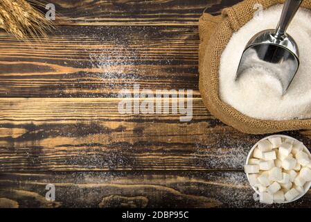 Zucchero bianco in sacco e ciotola su tavolo di legno, vista dall'alto Foto Stock